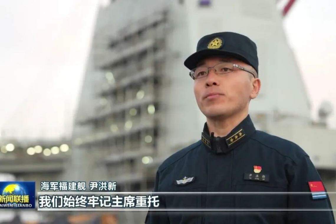 身穿戎装的尹洪新上校站在福建舰舰岛前受访。(《新闻联播》视频截屏)