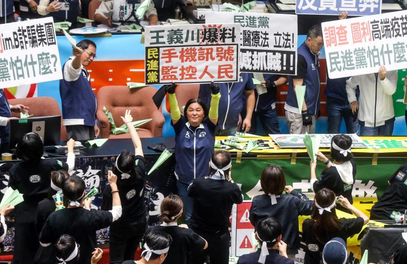 国民党立委陈玉珍(中)星期二在立法院内高举抗议字牌,批评民进党利用手机讯号监控人民。另一端民进党立委则向主席台上射出绿色纸飞机。(法新社)