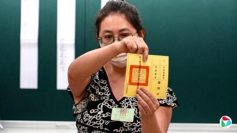 一名女士双手持有一张黄色选票,向前展示。