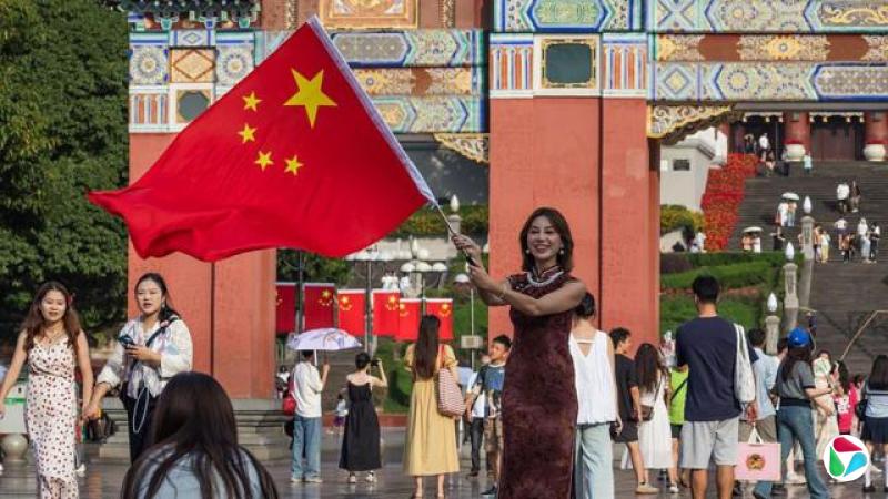 2025年10月7日国庆黄金周假期期间,一位女士在重庆人民大礼堂前挥舞着一面巨大的中国国旗,访客们汇聚于这一地标建筑。广场上遍布爱国装饰和红旗,人们共同庆祝中华人民共和国成立76周年。