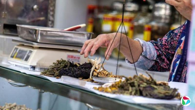 一位中医医师在药局为顾客配制各种中药。