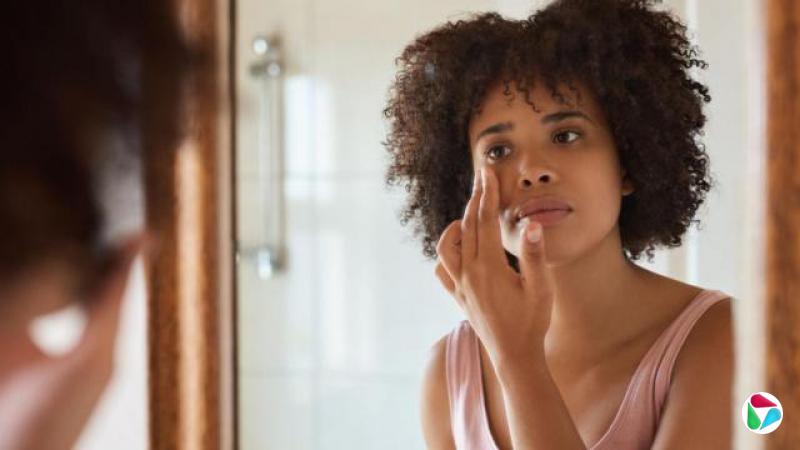 一位黑发年轻女子神情凝重地望着镜中的自己,双手轻触眼周的皮肤