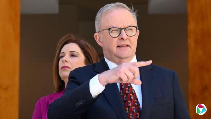 一名身穿西装、戴圆框眼镜的男子目光偏离镜头,一名穿粉红色西装外套的女子在他身后逼近