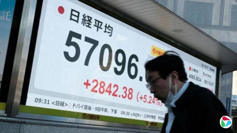 一名男子走过一块巨大的萤幕,萤幕上显示日经指数为57096点。