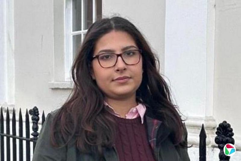 ������ķ?����Maryam Khan��վ�ڻ��⣬������һ����������Χ���Ľ����������ͷ΢Ц������۾������ŷۺ�ɫ����������ƺ�ɫ��ͷ������ɫ����