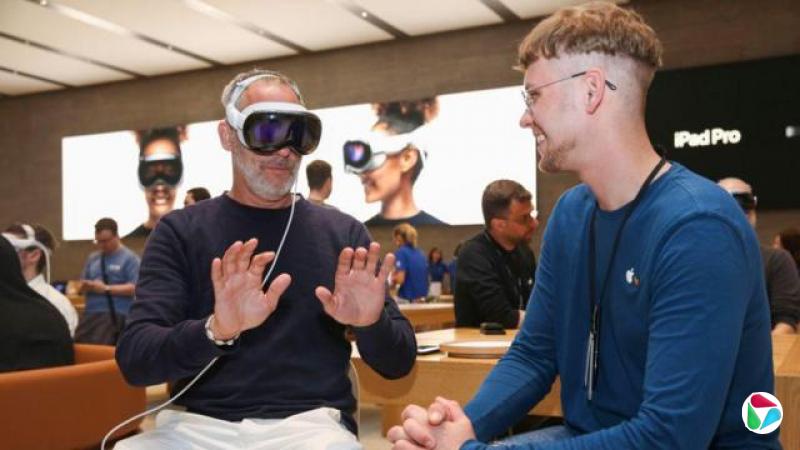 �¹�����ĳƻ��ר�����ڣ�һ���������ţ�ͷ�ϴ��Ű�ɫ Apple Vision Pro ����������͸����ɫ�����ӡ���˫������ǰ����һλƻ��Ա���������Աߣ�����΢Ц����2024��7�£�